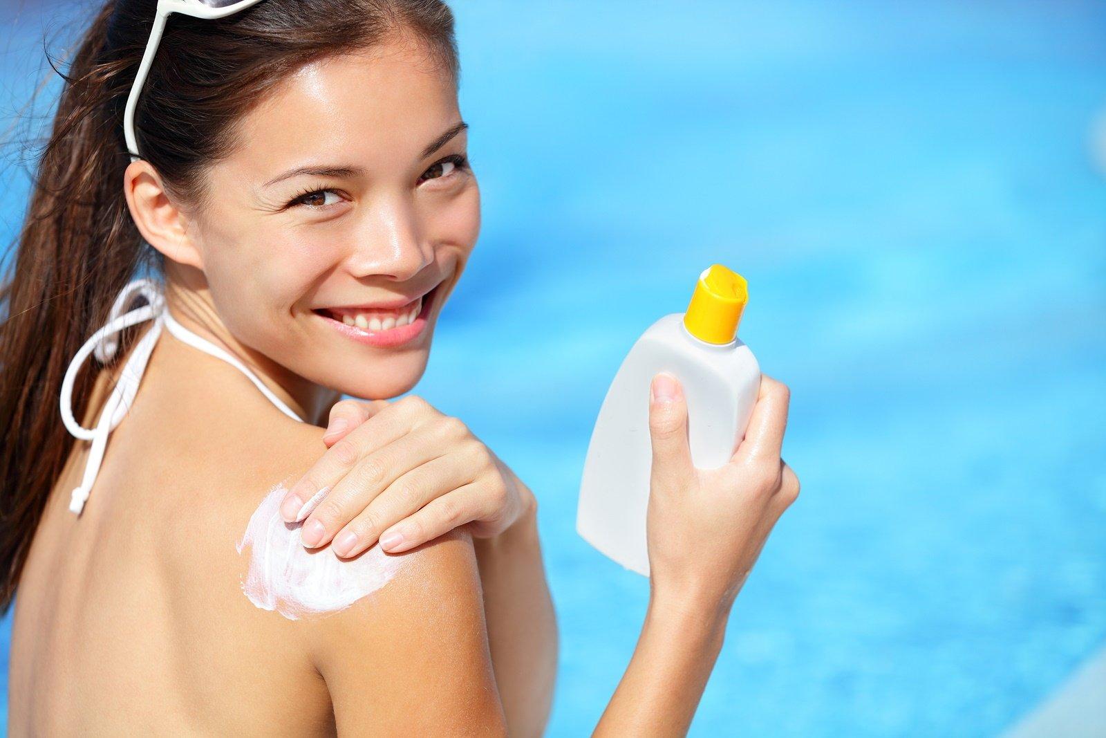 Sunscreen / sunblock. Woman putting solar cream on shoulder smil