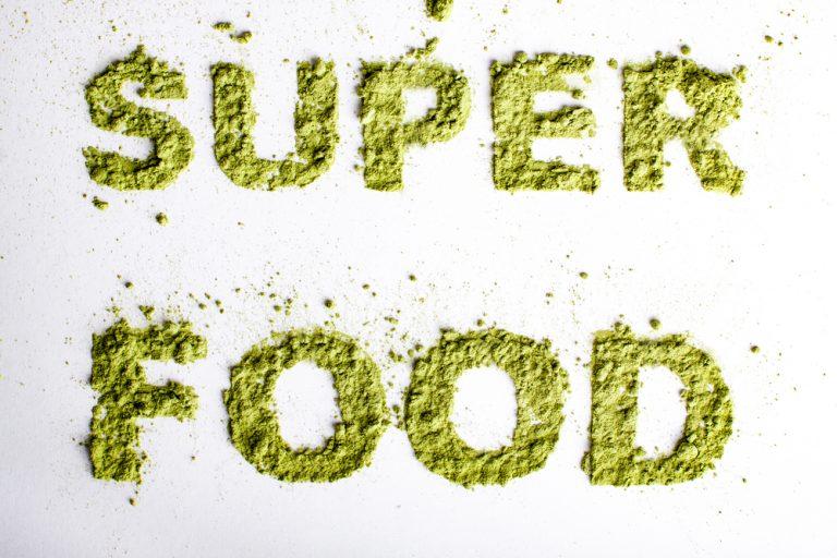 Word superfood piled of green powder of barley grass on white background.