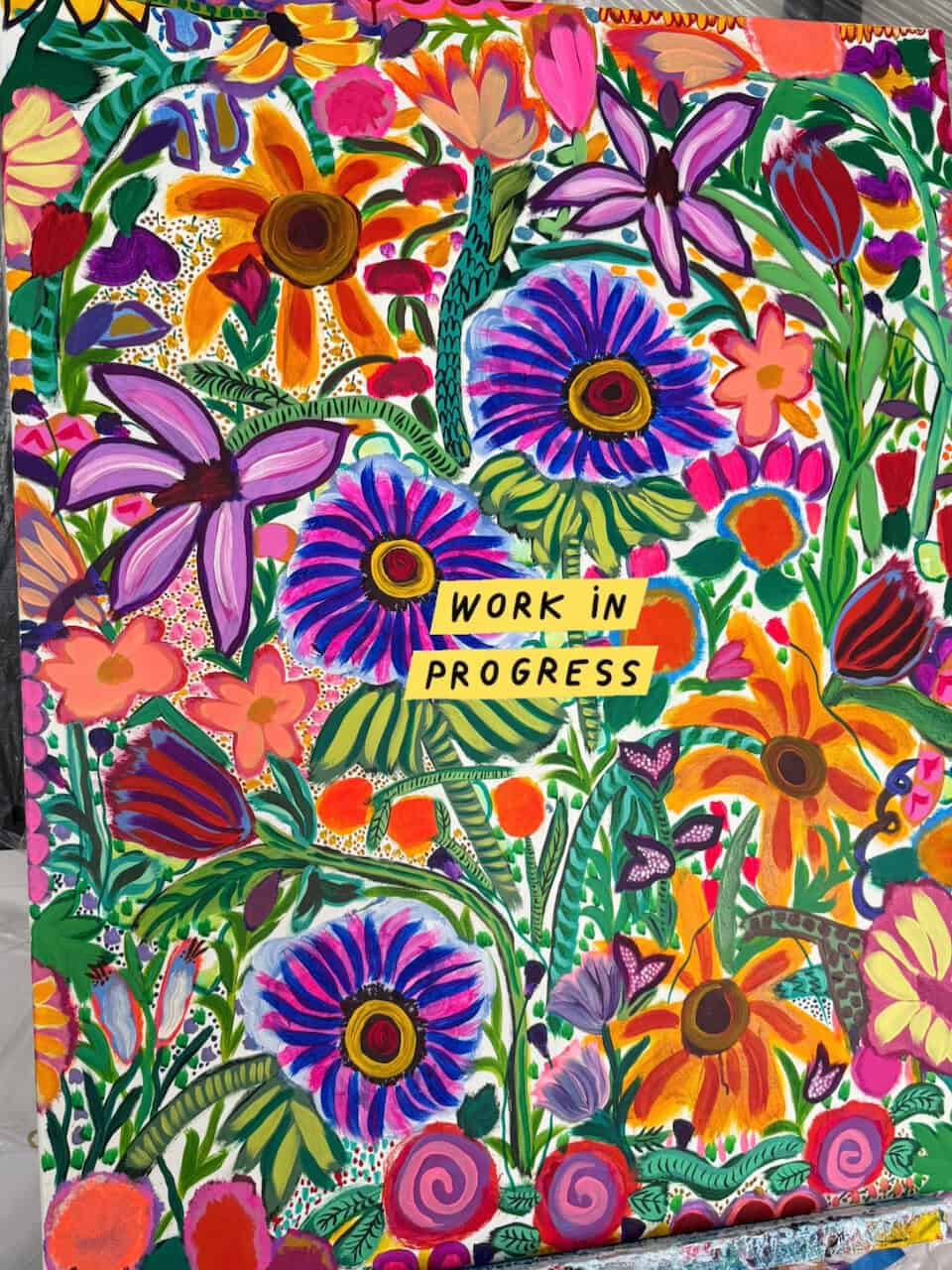 Vibrant floral mural with bold, colorful flowers and leaves, featuring yellow tape that reads 'WORK IN PROGRESS'